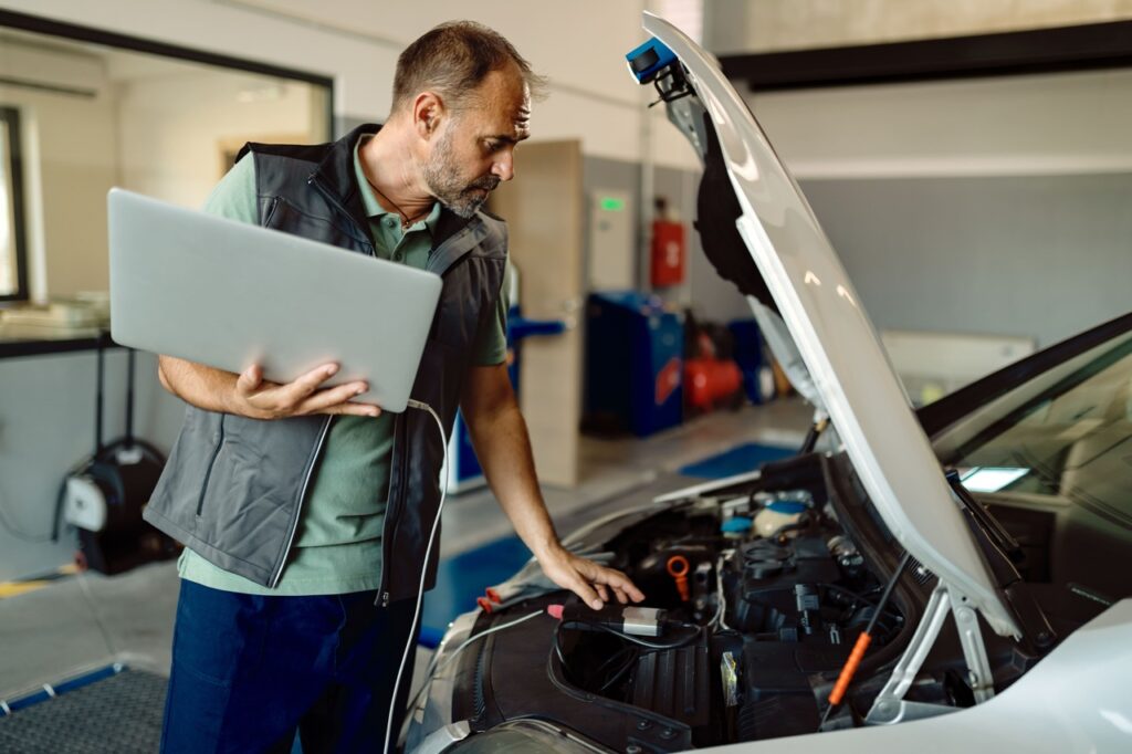 auto repairman using laptop while examining car engine workshop min Easy Resize.com